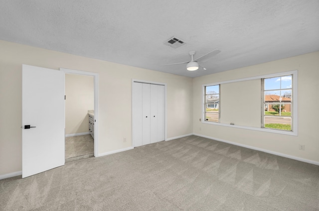 unfurnished bedroom featuring a closet, visible vents, light carpet, and a textured ceiling