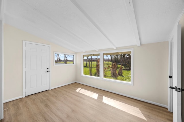 interior space featuring lofted ceiling with beams, light wood finished floors, baseboards, and a textured ceiling