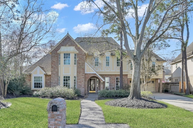 tudor-style house featuring brick siding, stucco siding, a shingled roof, a front yard, and driveway