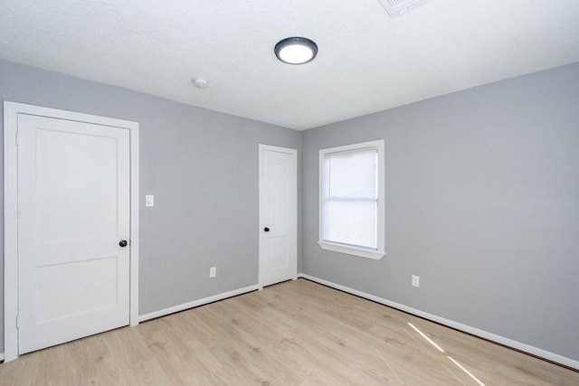 spare room with light wood-type flooring, visible vents, and baseboards