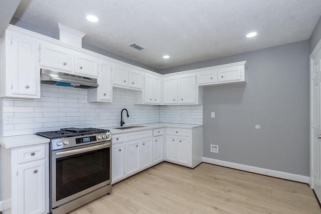 kitchen with light countertops, white cabinetry, a sink, stainless steel gas range, and under cabinet range hood