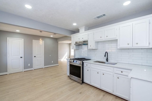 kitchen with under cabinet range hood, stainless steel gas range oven, a sink, and white cabinets