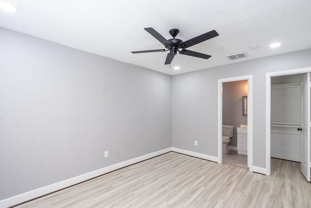 unfurnished bedroom featuring a walk in closet, a closet, visible vents, light wood-style flooring, and baseboards