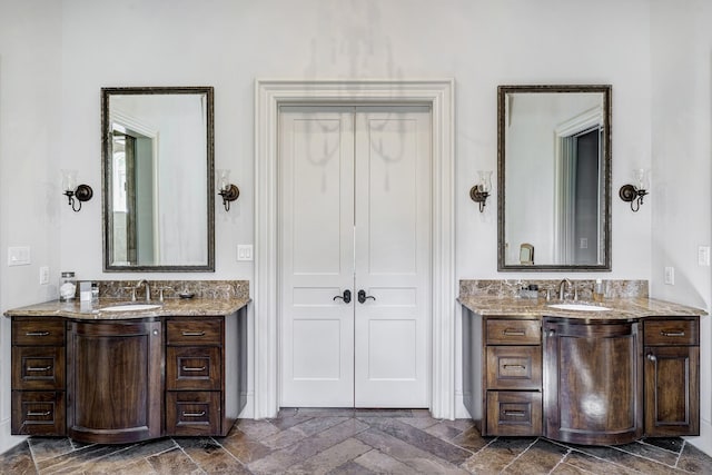 full bathroom featuring stone finish flooring, two vanities, and a sink