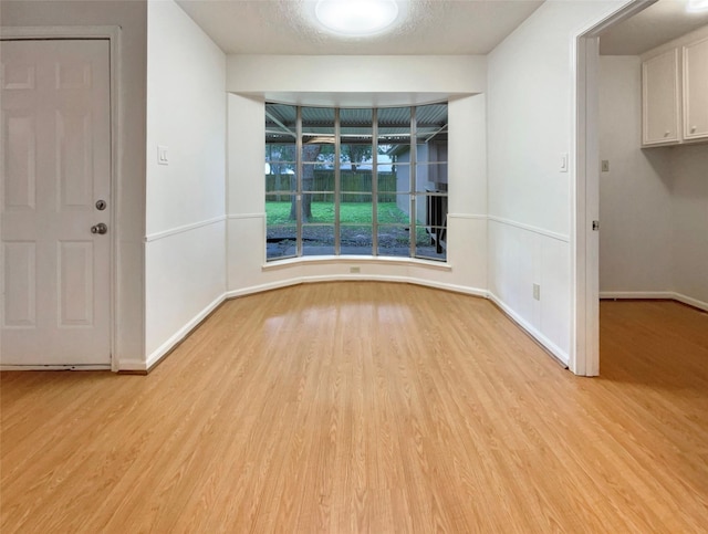 spare room with light wood-type flooring, baseboards, and a textured ceiling