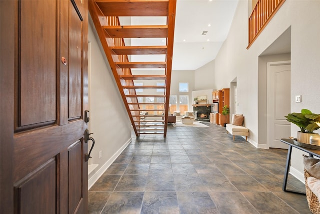 foyer entrance with a towering ceiling, a lit fireplace, stairway, and baseboards