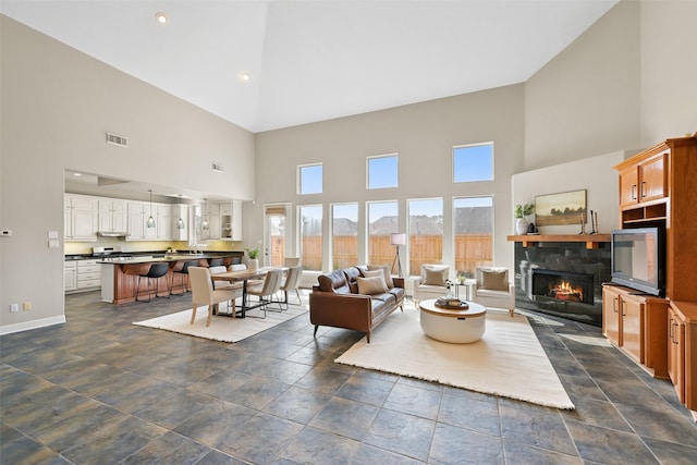 living area with visible vents, a fireplace, high vaulted ceiling, and baseboards