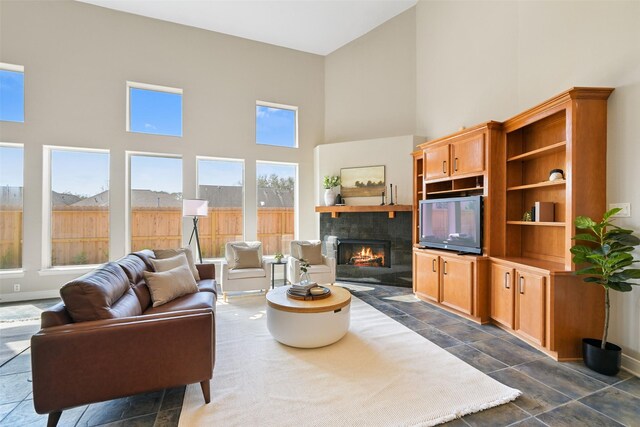 living room with a tiled fireplace, baseboards, a towering ceiling, and stone finish flooring