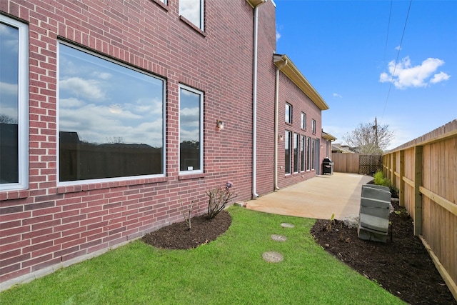 view of side of property with a patio area, a yard, a fenced backyard, and brick siding