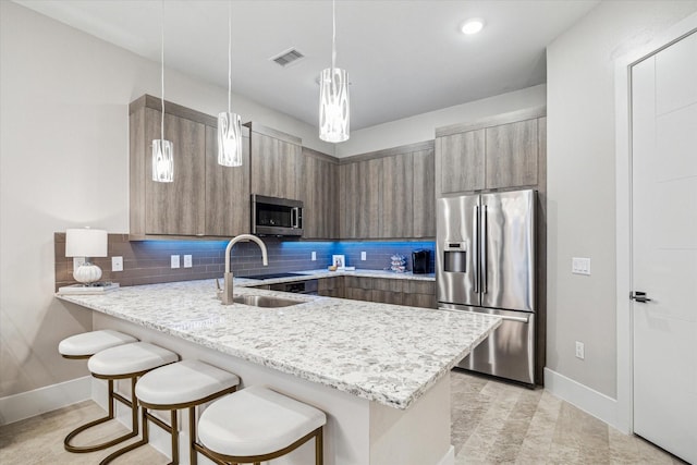 kitchen featuring hanging light fixtures, a peninsula, light stone counters, and stainless steel appliances