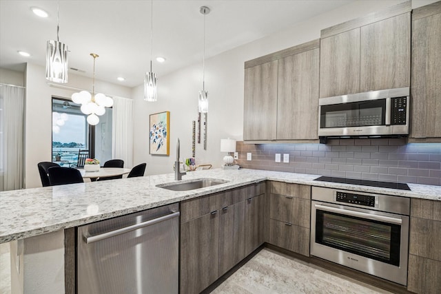 kitchen featuring tasteful backsplash, appliances with stainless steel finishes, light stone counters, a peninsula, and a sink