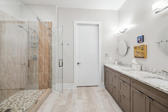 bathroom with double vanity, wood finished floors, a stall shower, and a sink