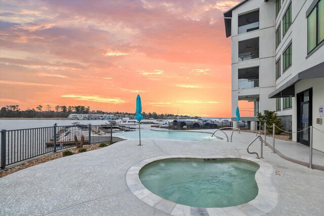 pool at dusk with fence and a hot tub