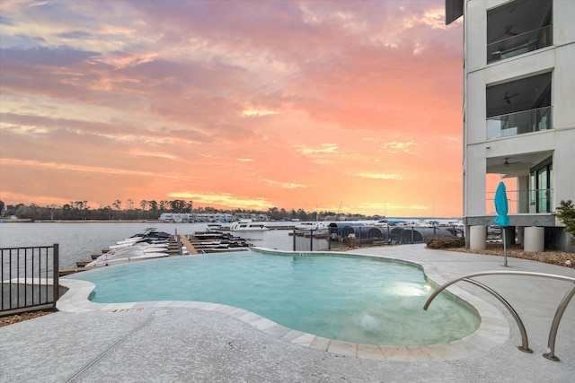 pool at dusk with an infinity pool, a patio, and a water view