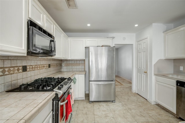 kitchen featuring visible vents, decorative backsplash, tile counters, appliances with stainless steel finishes, and white cabinetry