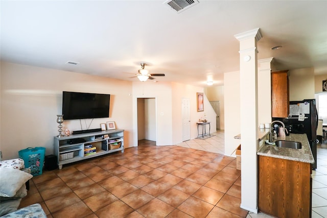 tiled living area featuring ceiling fan, decorative columns, a sink, and visible vents