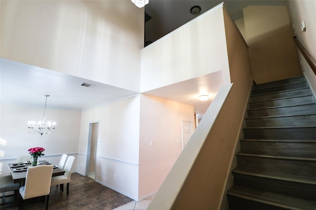 stairs featuring visible vents, a towering ceiling, wood finished floors, an inviting chandelier, and crown molding