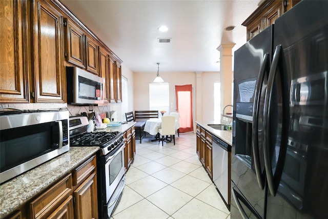 kitchen with light tile patterned flooring, a sink, appliances with stainless steel finishes, decorative light fixtures, and ornate columns