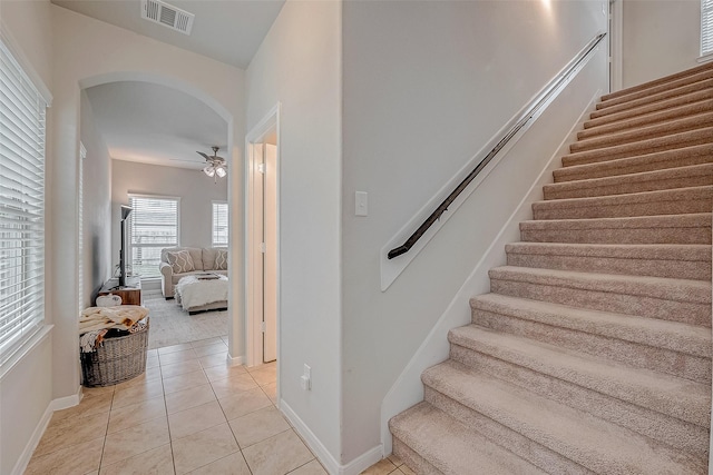 staircase featuring visible vents, arched walkways, baseboards, ceiling fan, and tile patterned floors