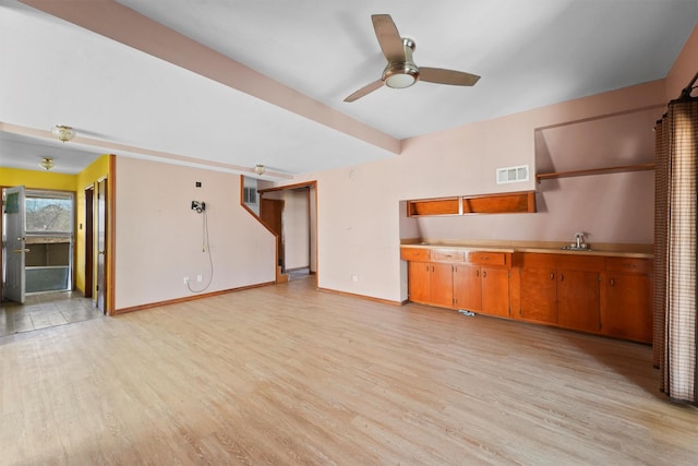 unfurnished living room featuring baseboards, visible vents, beamed ceiling, light wood-type flooring, and a sink