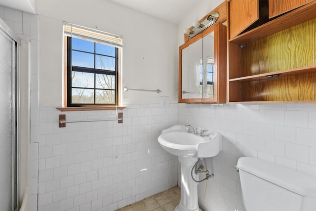 bathroom with toilet, a wainscoted wall, tile walls, and a shower with shower door