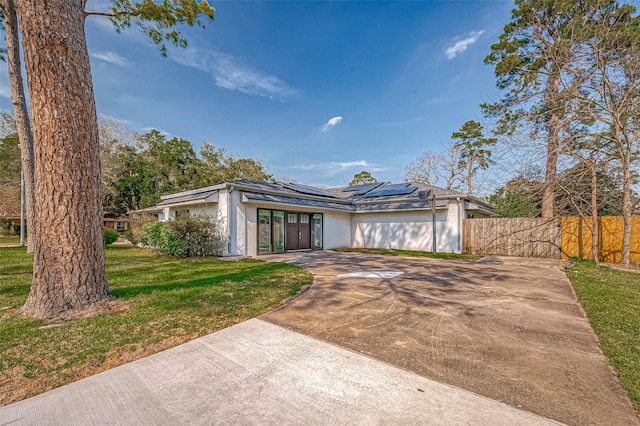 mid-century modern home featuring solar panels, stucco siding, concrete driveway, a front yard, and fence