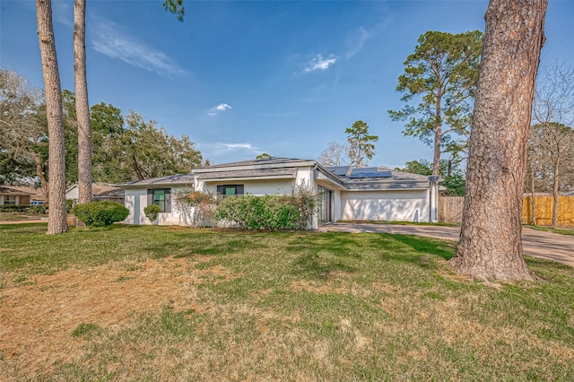 view of front of property with concrete driveway, a front lawn, and roof mounted solar panels