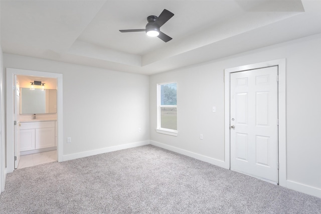 unfurnished bedroom featuring light carpet, ensuite bath, baseboards, and a raised ceiling