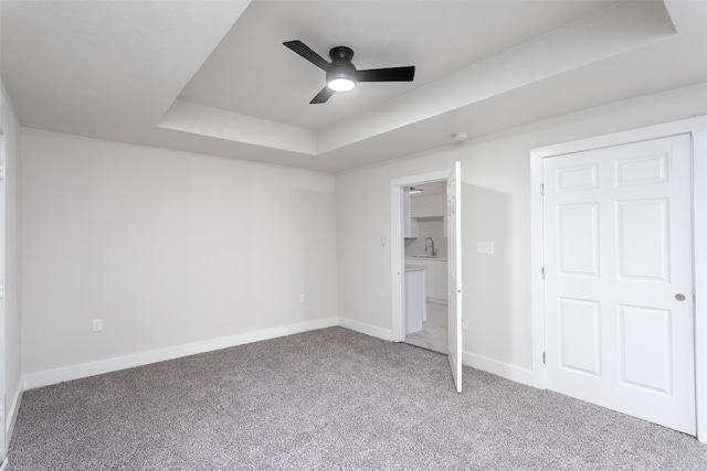 unfurnished bedroom featuring ceiling fan, carpet, a raised ceiling, and baseboards