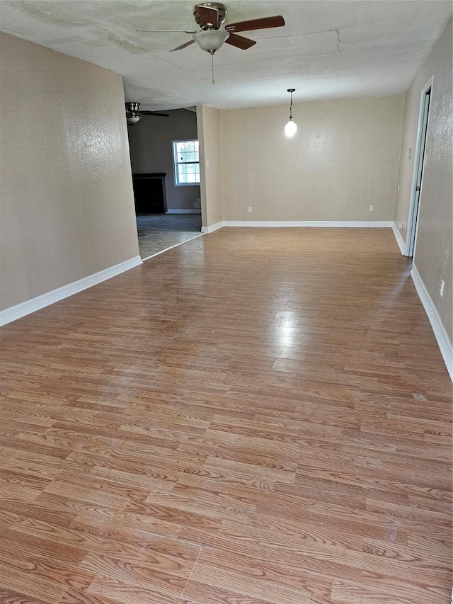 empty room featuring light wood finished floors, baseboards, and a ceiling fan