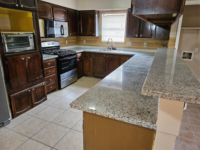 kitchen featuring black microwave, a peninsula, a sink, light stone countertops, and stainless steel gas stove