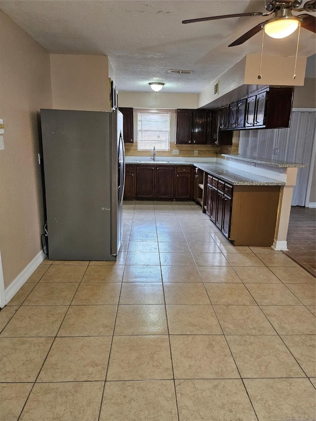 kitchen with light tile patterned floors, visible vents, freestanding refrigerator, a sink, and dark brown cabinetry