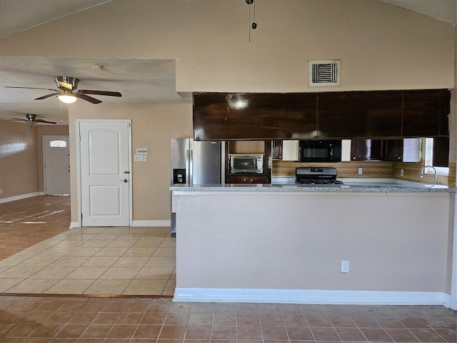 kitchen with black microwave, vaulted ceiling, stove, and stainless steel fridge