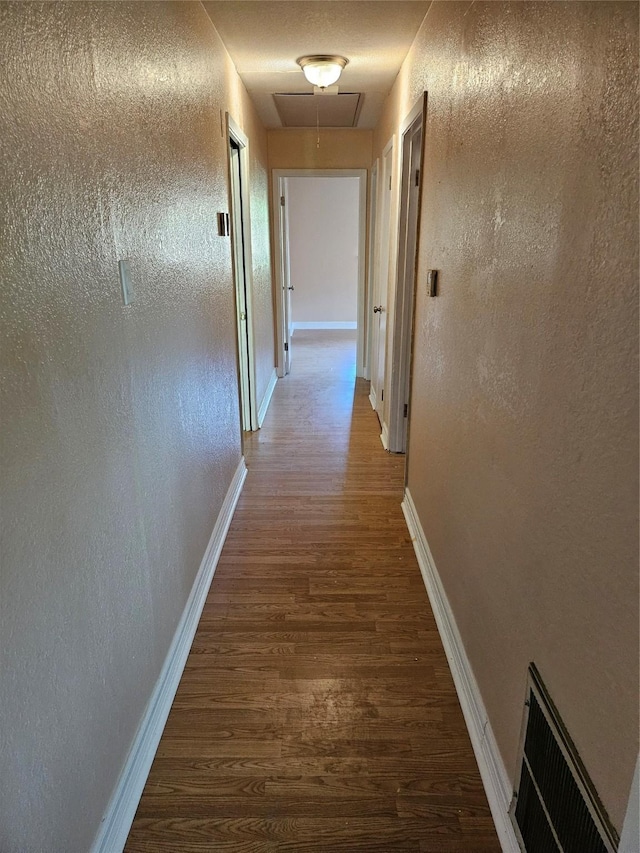 hall with attic access, visible vents, dark wood finished floors, and baseboards