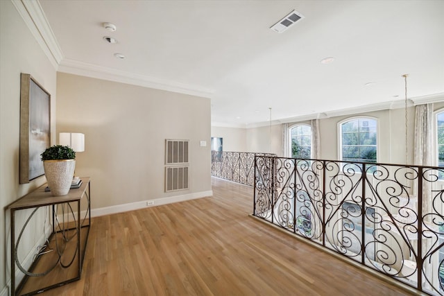 corridor featuring ornamental molding, light wood-type flooring, visible vents, and baseboards