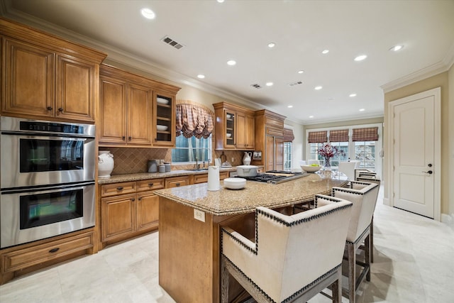 kitchen with double oven, visible vents, a center island, a kitchen bar, and glass insert cabinets