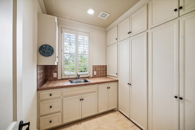 kitchen with tile countertops, tasteful backsplash, visible vents, and a sink