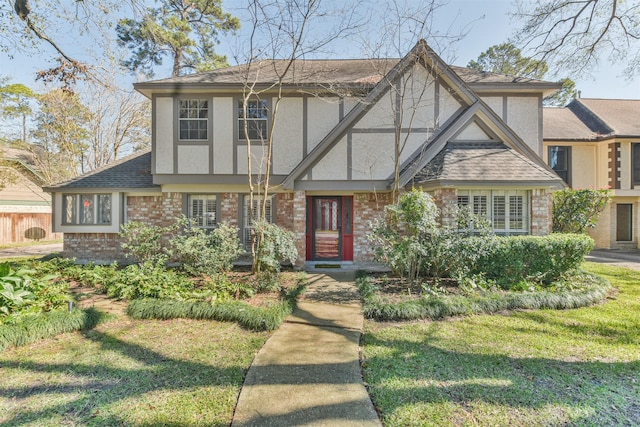 tudor home featuring brick siding, a shingled roof, a front lawn, and stucco siding