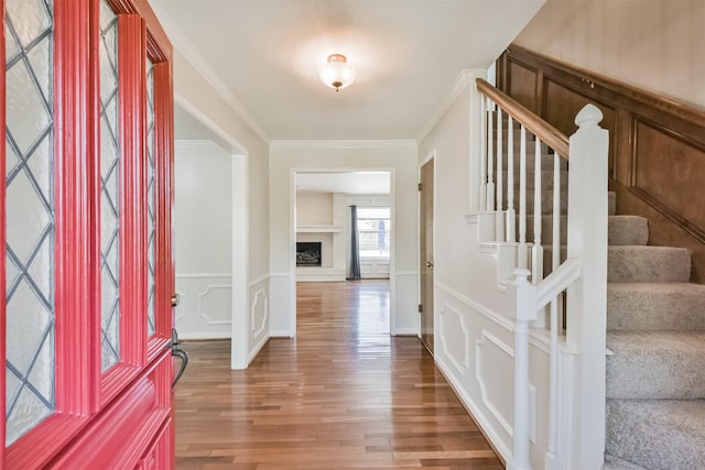 entrance foyer with stairway, wood finished floors, crown molding, a brick fireplace, and a decorative wall