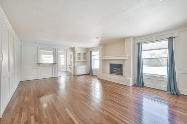 unfurnished living room with a textured ceiling, a brick fireplace, wood finished floors, and a decorative wall