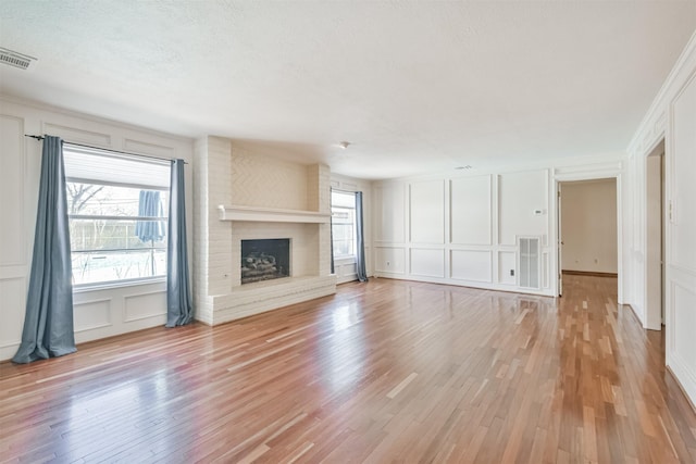 unfurnished living room featuring a wealth of natural light, light wood-style floors, visible vents, and a decorative wall