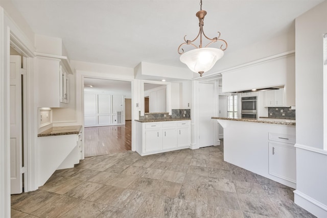 kitchen featuring a peninsula, double oven, white cabinetry, pendant lighting, and backsplash