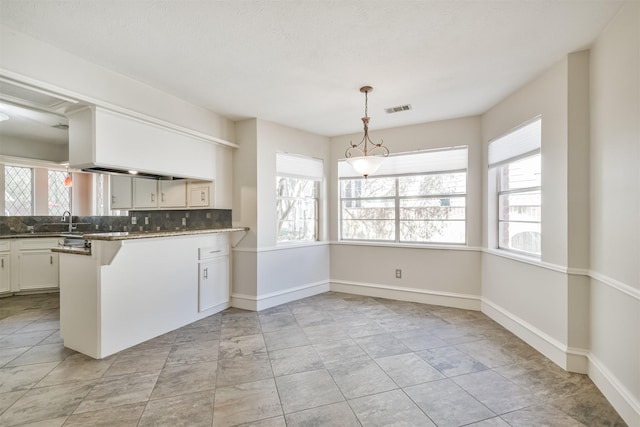 kitchen with visible vents, dark countertops, a peninsula, white cabinetry, and pendant lighting