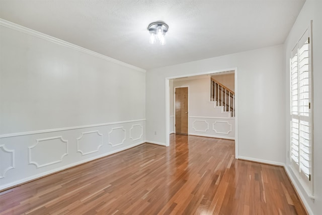 unfurnished room with crown molding, a decorative wall, stairway, wainscoting, and wood finished floors