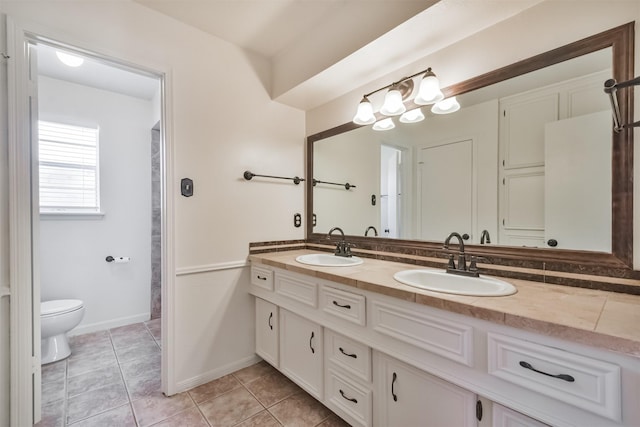 bathroom with double vanity, tile patterned flooring, toilet, and a sink