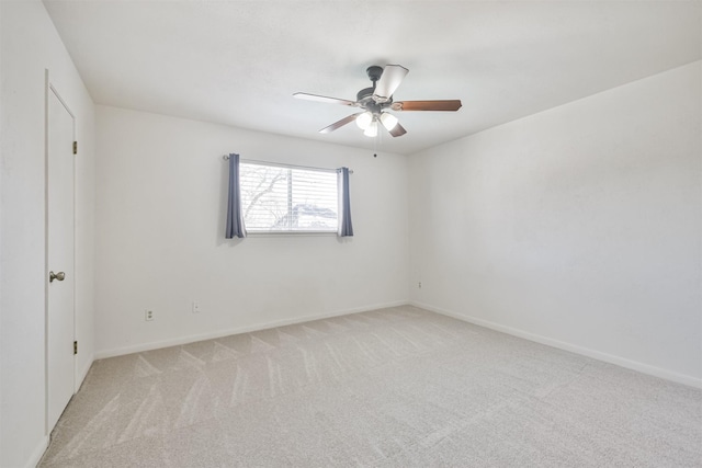 empty room featuring a ceiling fan, light colored carpet, and baseboards