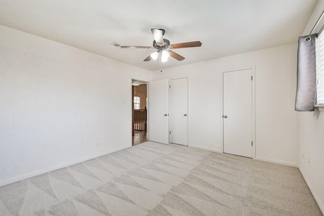 unfurnished bedroom with light carpet, a ceiling fan, baseboards, and multiple closets