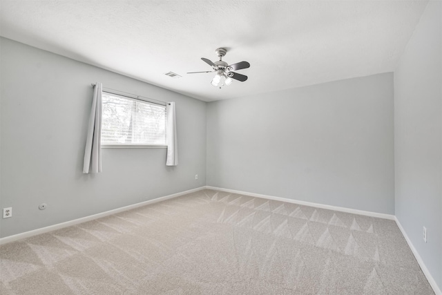 carpeted spare room featuring a ceiling fan, visible vents, and baseboards