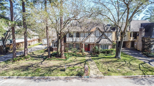 english style home featuring brick siding, fence, and a front lawn