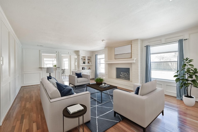 living room with a textured ceiling, a fireplace, a decorative wall, and wood finished floors